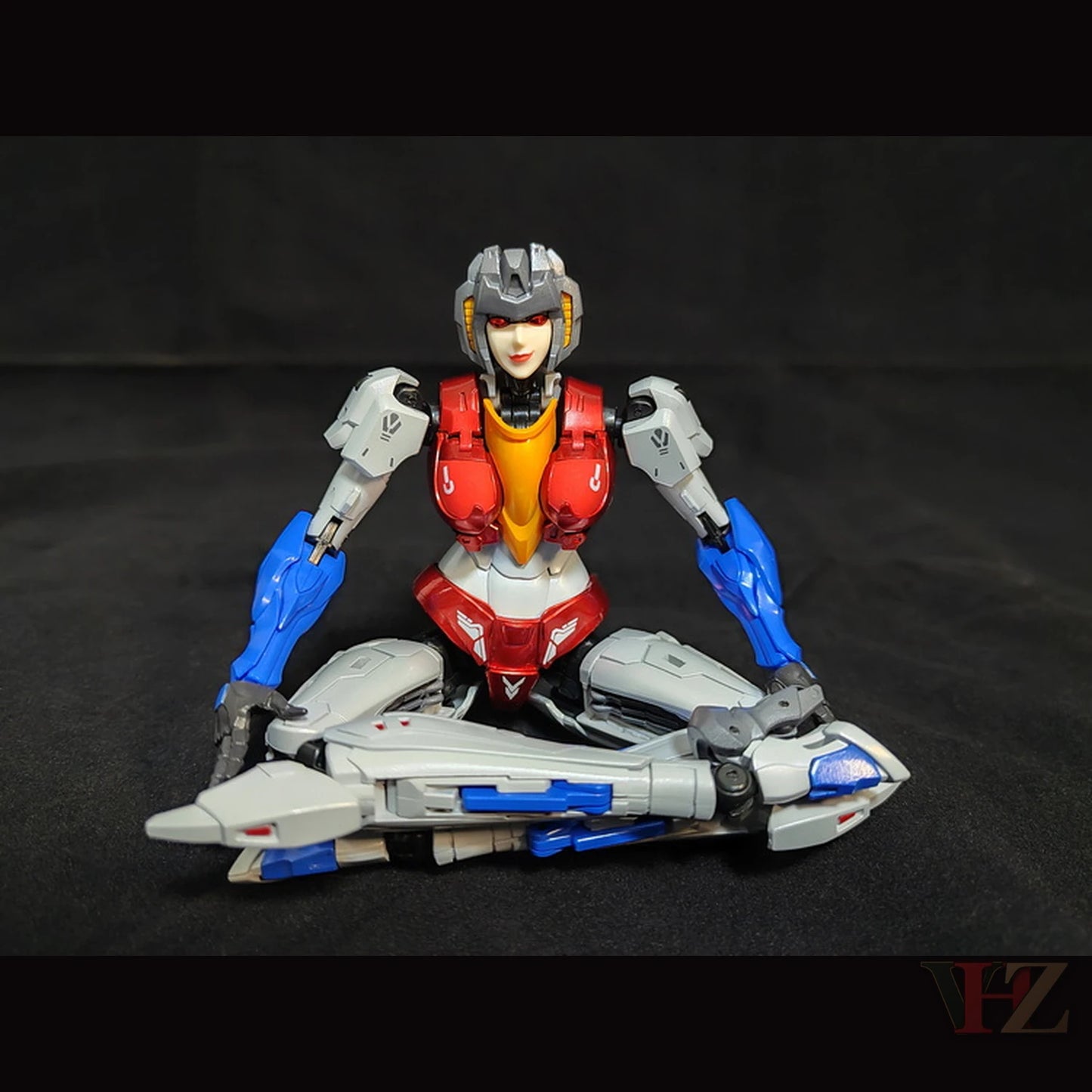 Collection Space CS-03 Starqueen Starscream Mecha Girl sitting cross-legged with jet mode, white/red/blue body, against black.