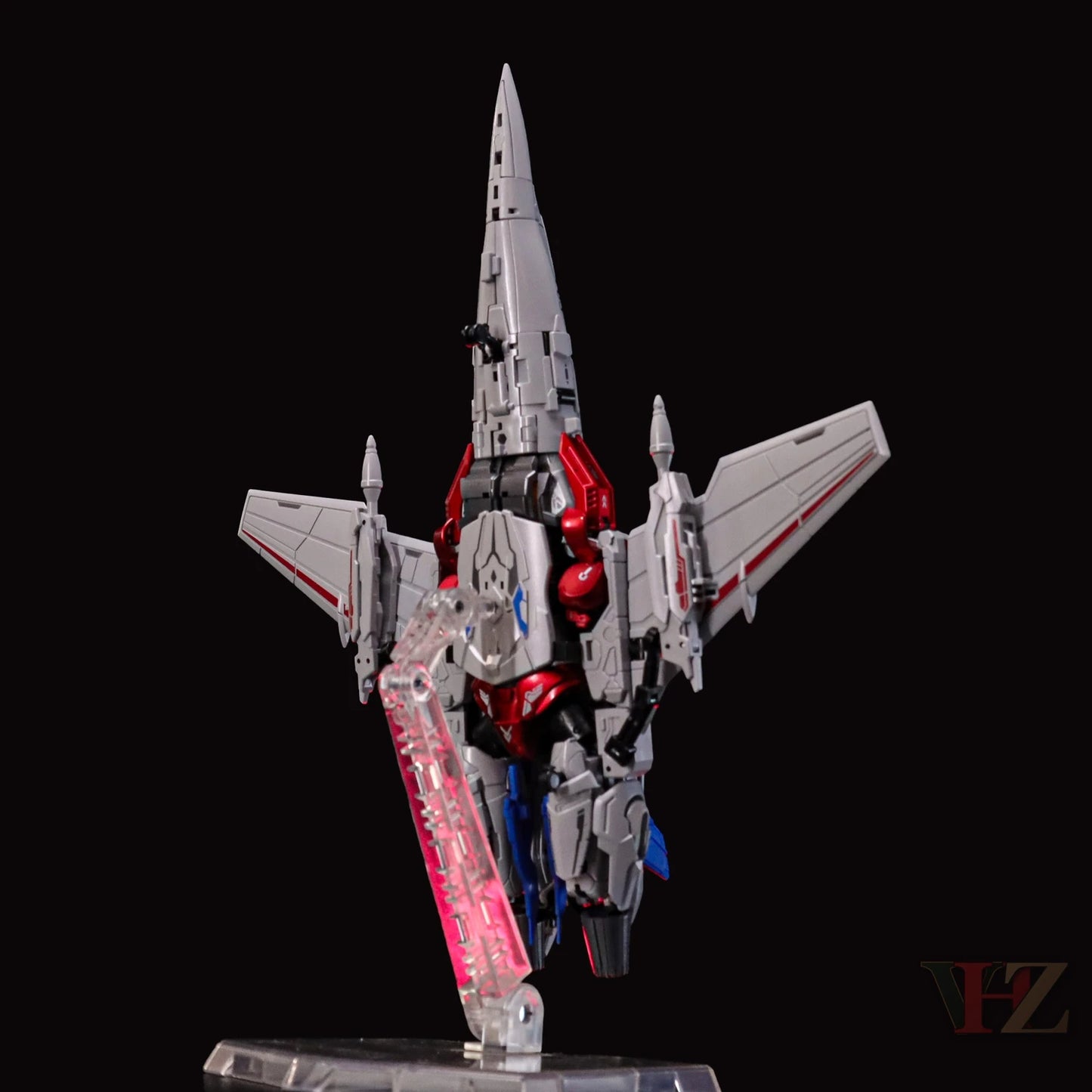 Angled rear view of Collection Space CS-03 Starqueen Starscream jet mode figure, silver with red and blue details, mechanical components, on clear stand with pink accents.